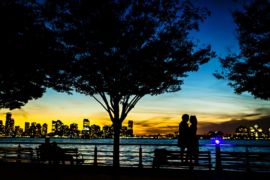 An engaged lesbian couple embrace along the water on the west side of Manhattan at sunset.
